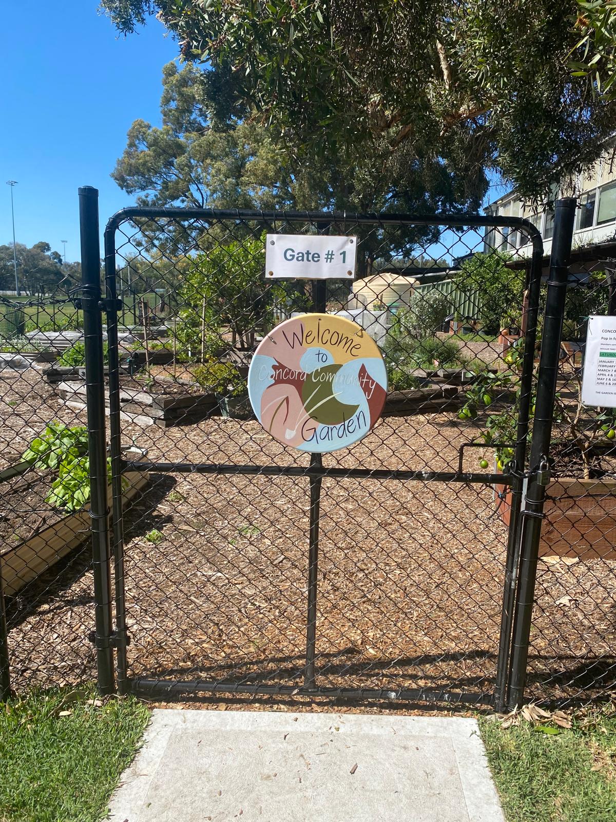 Gate 1 entrance to Concord Community Garden with the hand-painted welcome sign